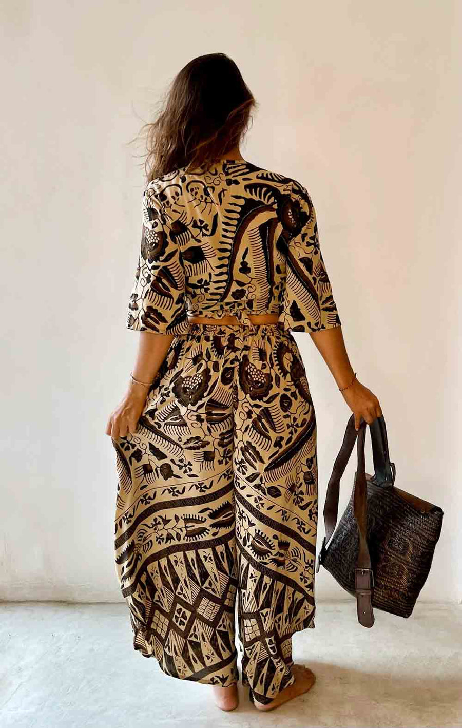 Woman wearing a patterned outfit holding a matching bag against a plain background