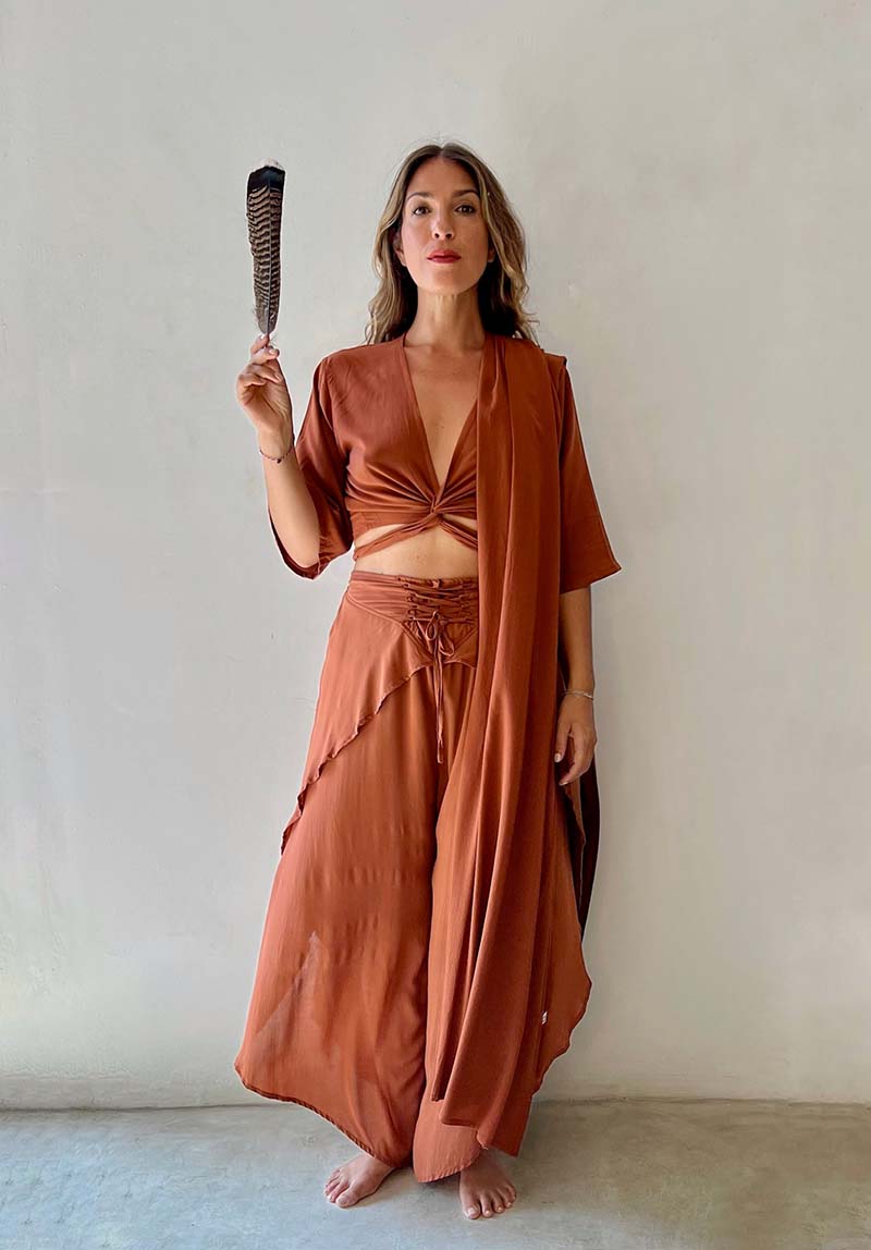 Woman in a rust-colored outfit holding a hairbrush against a plain background