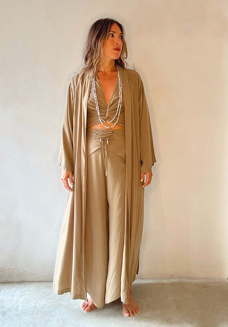 Woman wearing a beige satin outfit with a long robe against a plain background