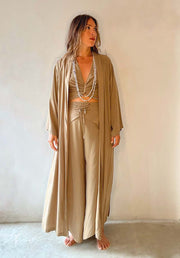 Woman wearing a beige satin outfit with a long robe against a plain background