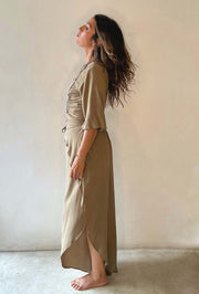 Woman wearing a long, light brown dress against a plain background