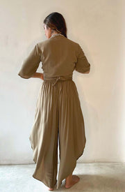 Woman wearing a green jumpsuit standing against a plain white wall.