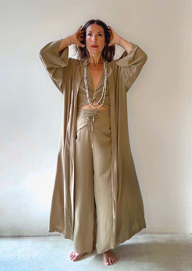 Woman wearing a beige outfit with a long duster and wide-leg pants against a plain background