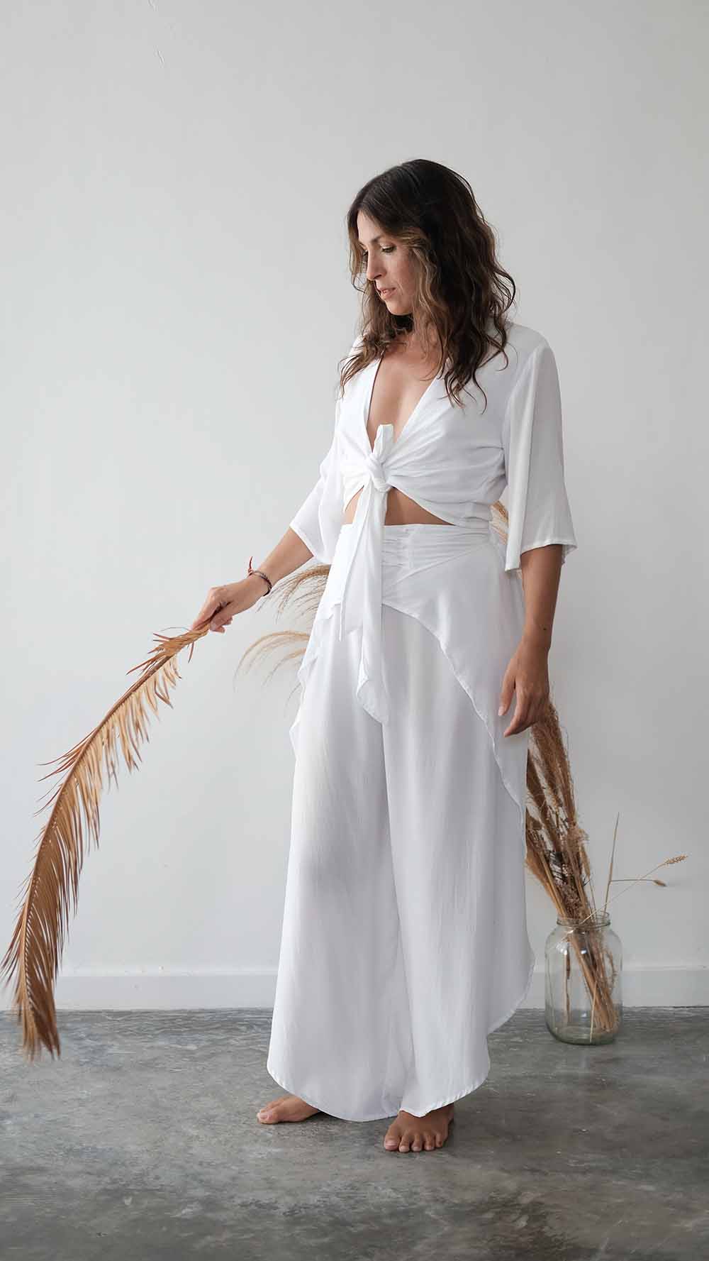 Woman wearing a white outfit holding dried palm leaves against a plain background