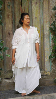 Woman wearing a white outfit standing in front of a rustic wooden door.
