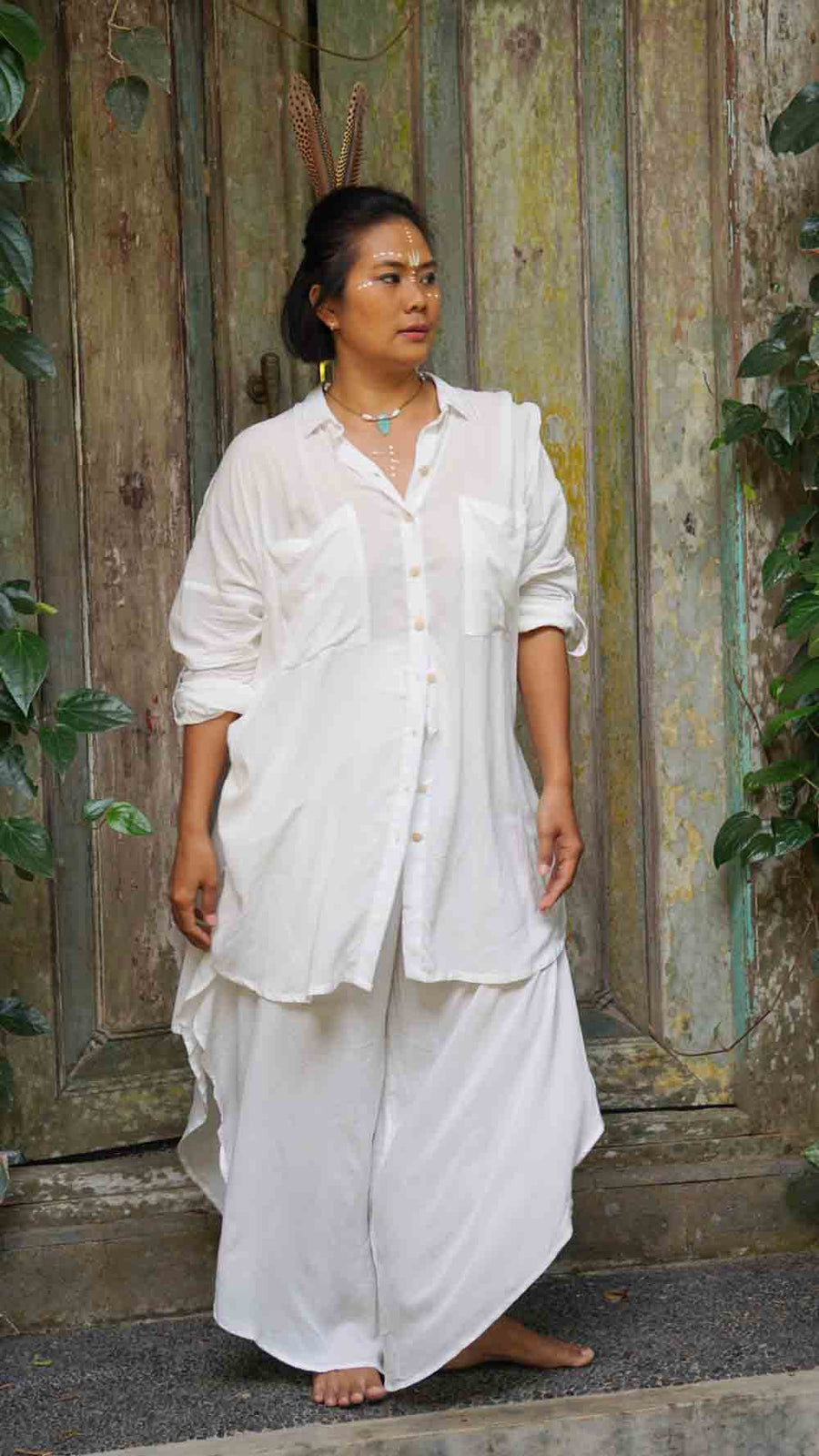 Woman wearing a white outfit standing in front of a rustic wooden door.