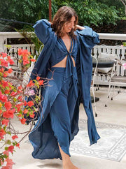 Woman in a blue outfit standing outdoors with flowers and furniture in the background