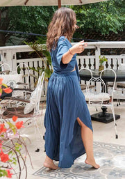 Woman in a blue dress standing on a patio with outdoor furniture and greenery.
