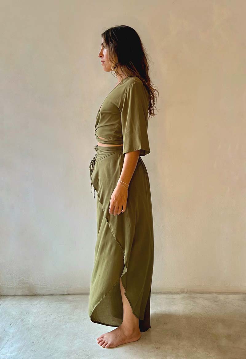 Woman wearing an olive green outfit standing against a plain wall.