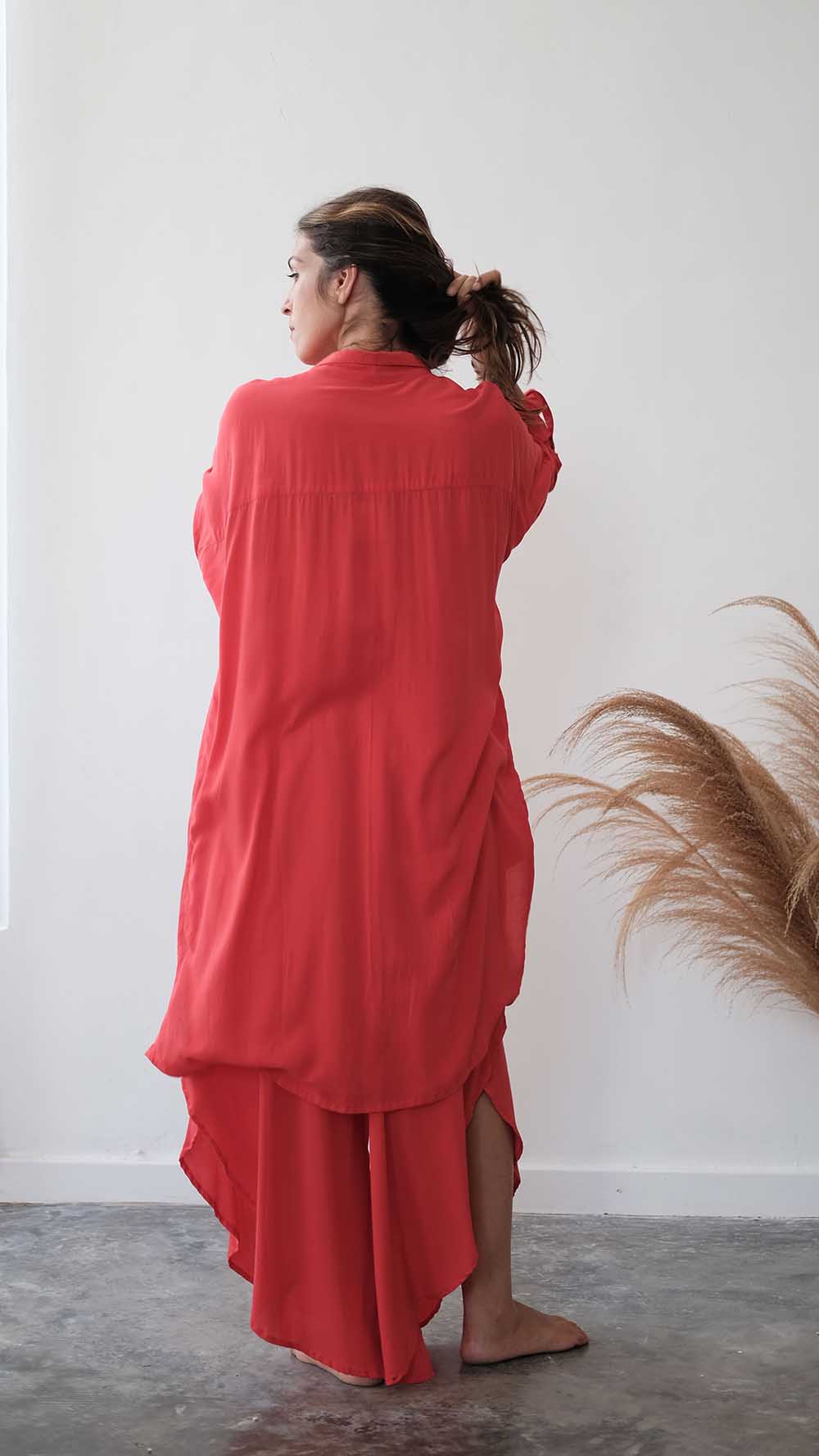 Person wearing a red outfit standing against a white wall with a plant to the side.