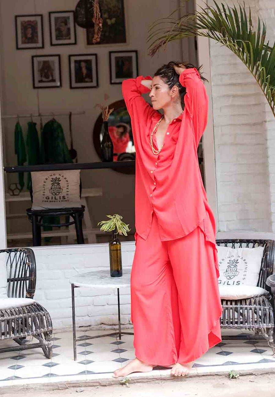 Woman in coral pajama set standing in a room with decor elements.