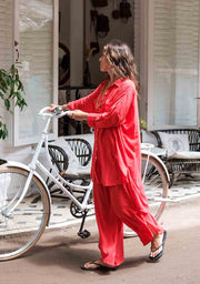 Woman in a red outfit standing next to a white bicycle on a street.