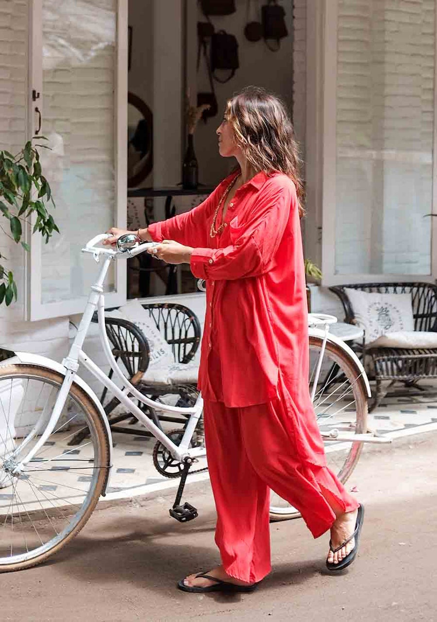 Woman in a red outfit standing next to a white bicycle on a street.