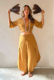 Woman in mustard yellow outfit holding feathers against a plain background
