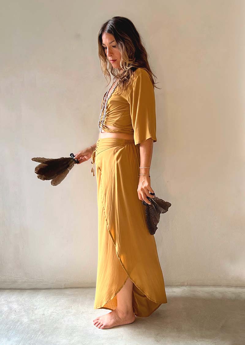Woman in a mustard yellow dress holding a brown bag against a plain background