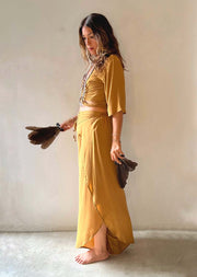Woman in a mustard yellow dress holding a brown bag against a plain background
