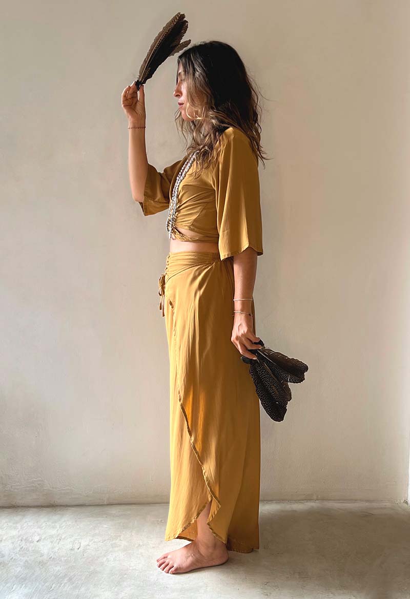 Woman in a mustard yellow outfit holding a feather duster against a plain background