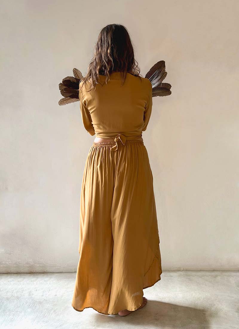 Person wearing a mustard yellow dress standing against a plain wall.