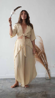 Woman in a beige dress holding a broom against a white wall