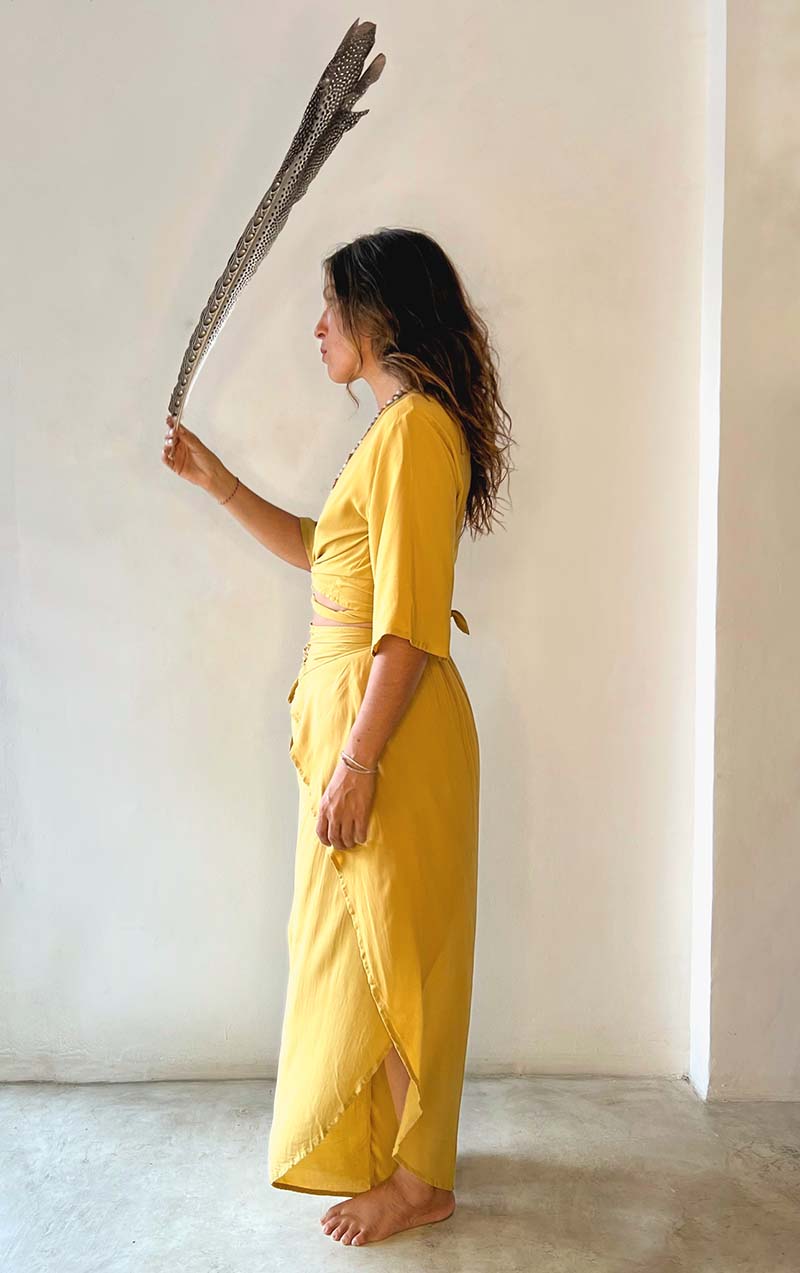 Person in a yellow dress holding a long stick against a white wall