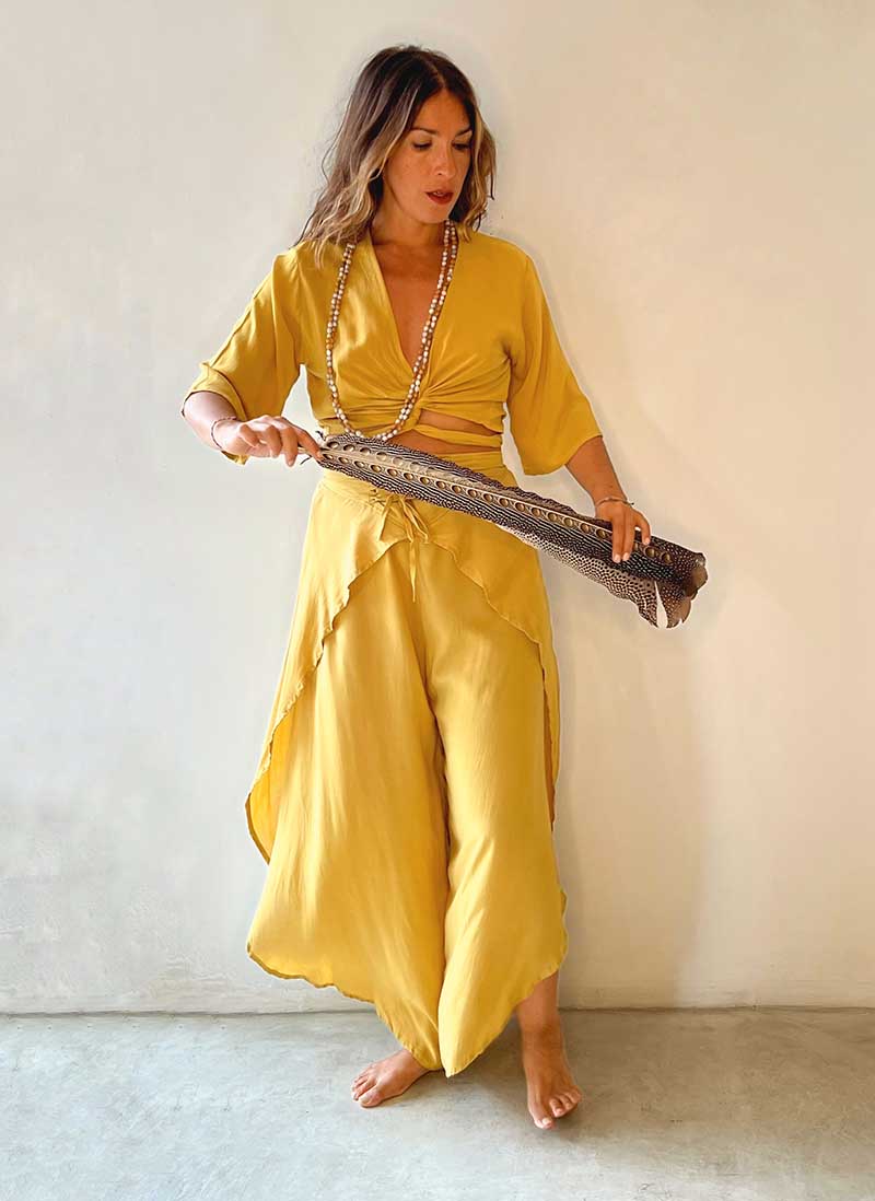 Woman in a yellow outfit holding a traditional stringed instrument against a plain background