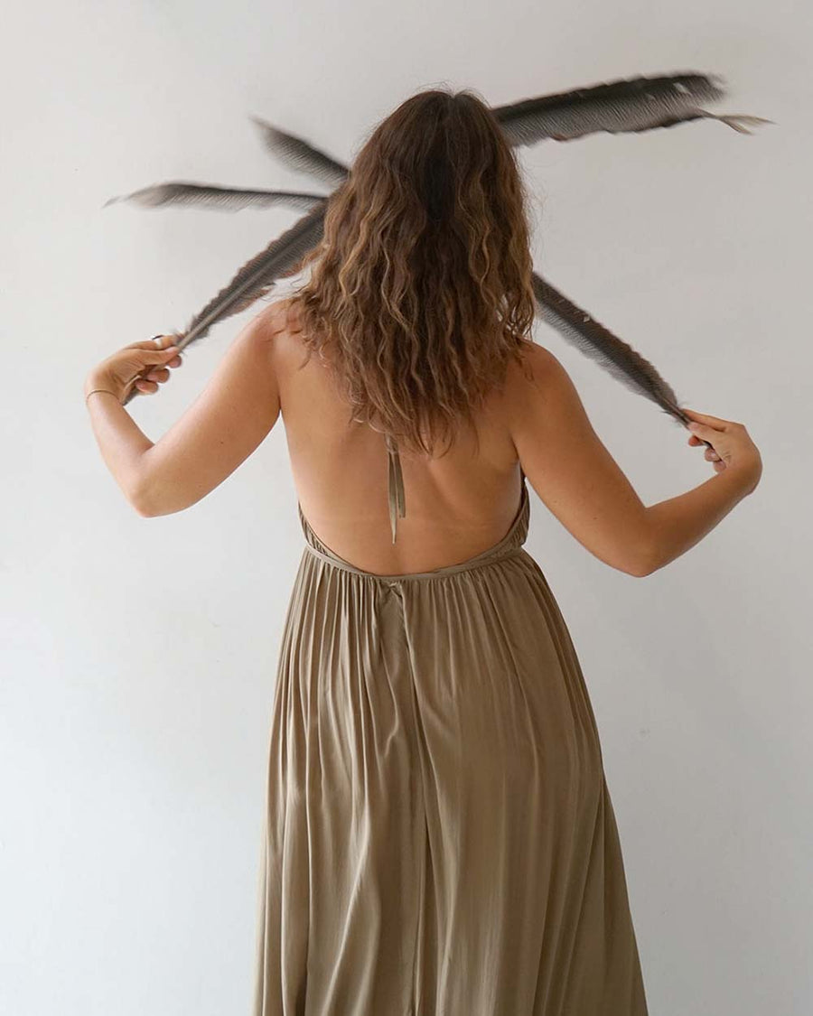 Woman in a beige dress holding feathers against a plain background
