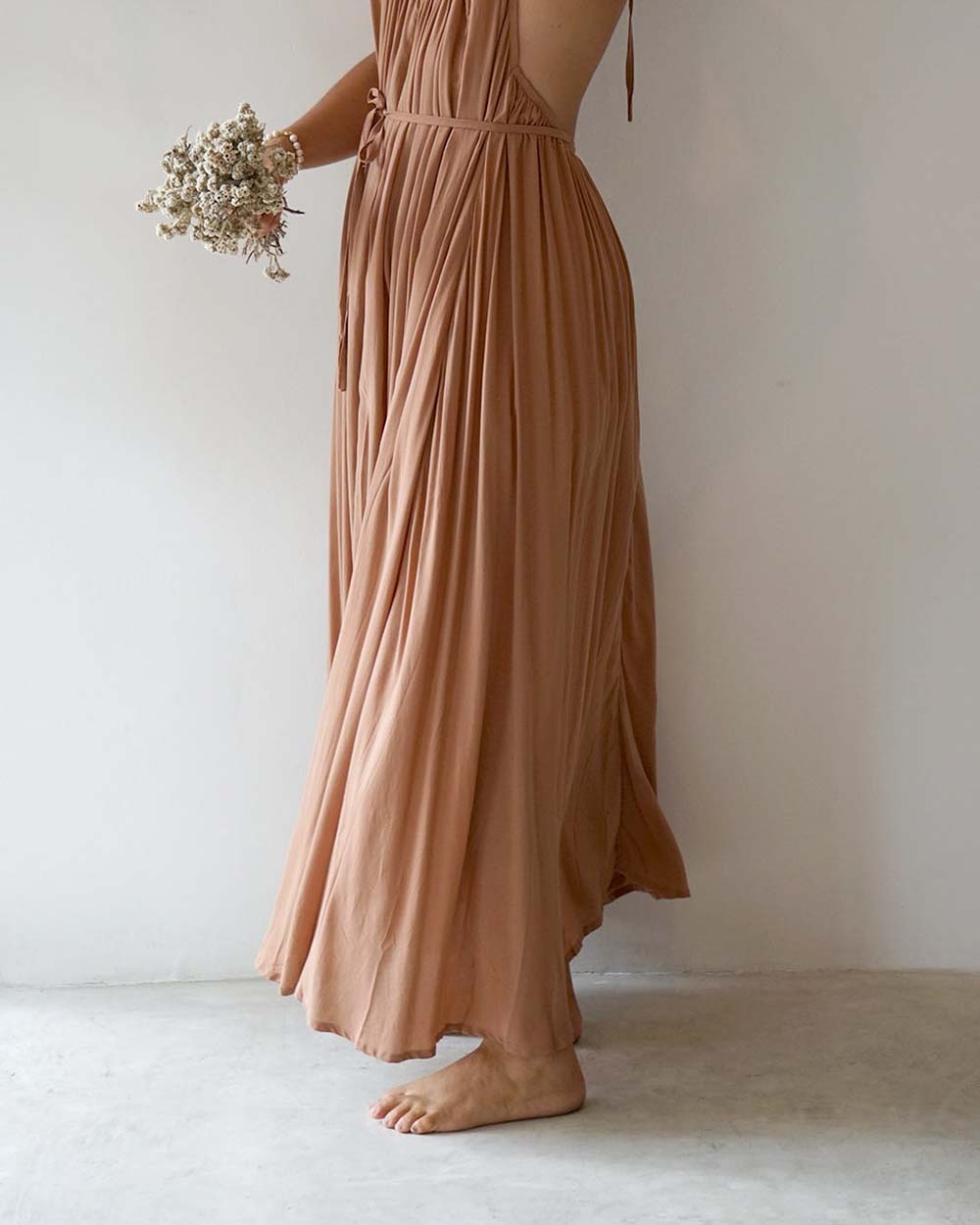 Person wearing a long, flowing brown dress holding dried flowers against a plain background