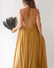 Woman in a mustard yellow dress with an open back, holding a black fan against a white background