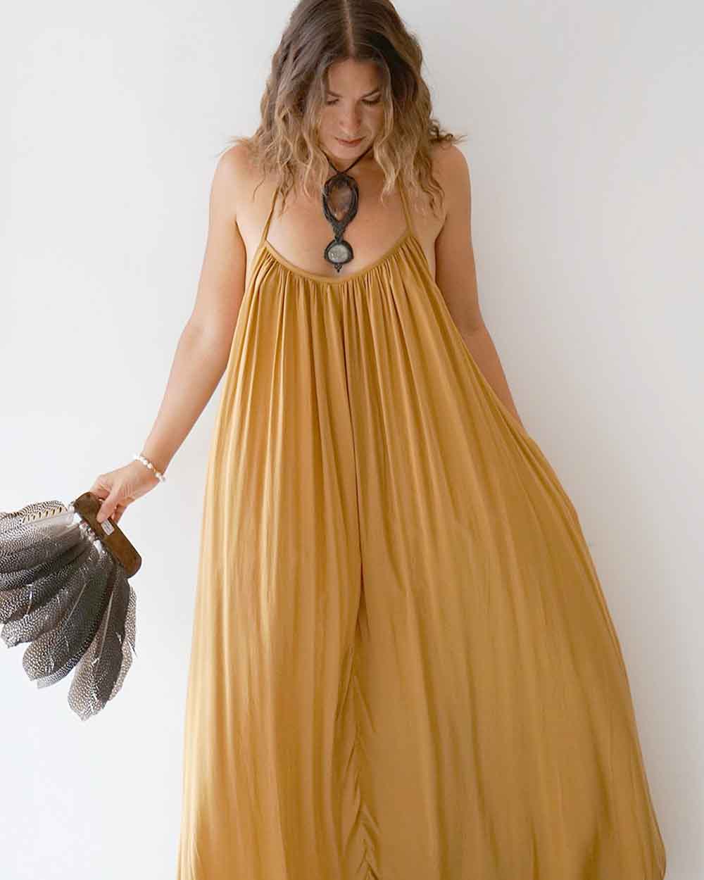Woman wearing a mustard yellow dress holding a gray clutch against a white background