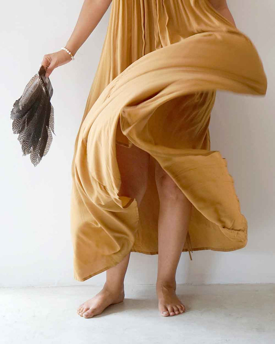 Person wearing a flowing mustard yellow dress holding a feather against a white background