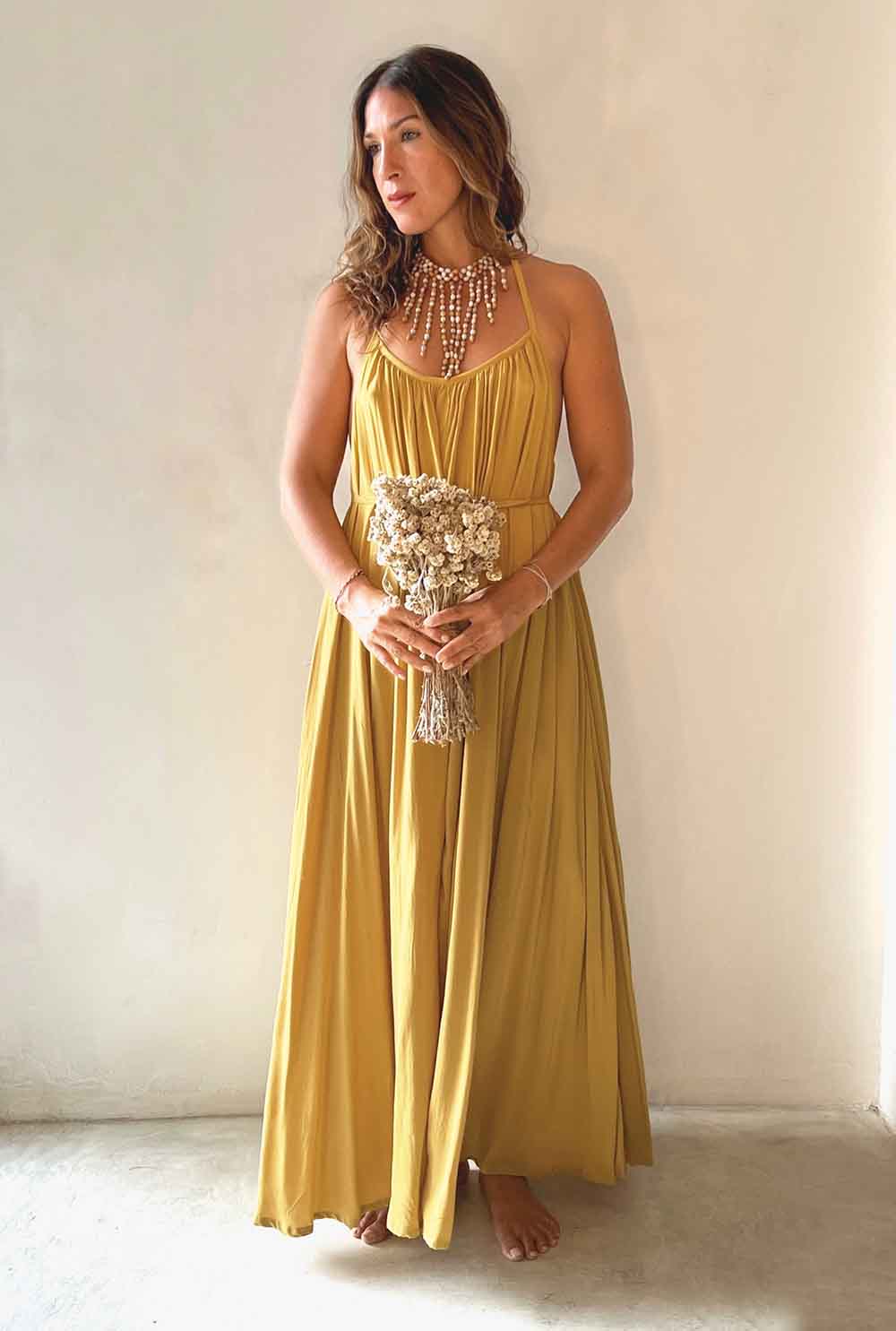 Woman in a yellow dress holding flowers against a plain background