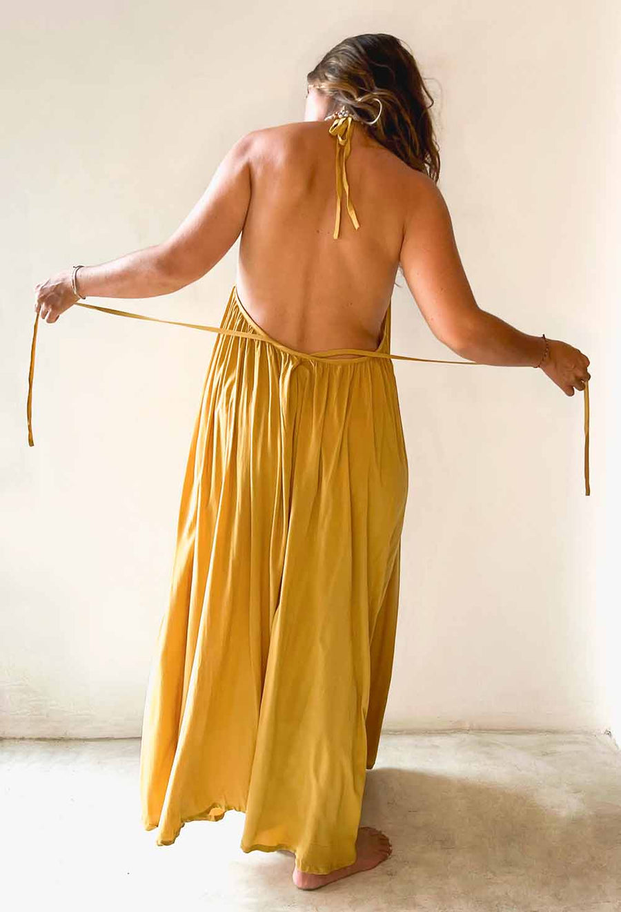 Woman wearing a mustard yellow dress with a halter neck design, holding the straps.