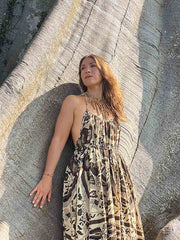 Woman in a patterned dress leaning against a large rock.