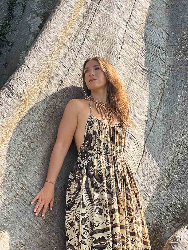 Woman in a patterned dress leaning against a large rock.
