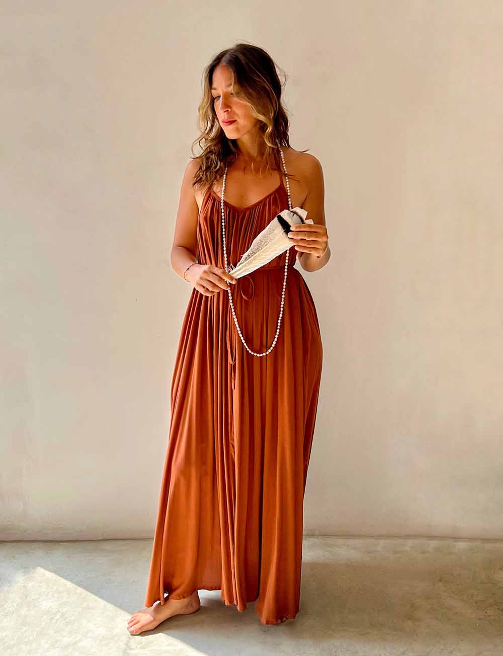 Woman wearing a rust-colored dress holding a book against a plain background