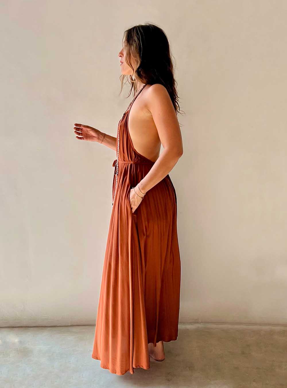 Woman wearing a rust-colored halter neck dress against a plain background