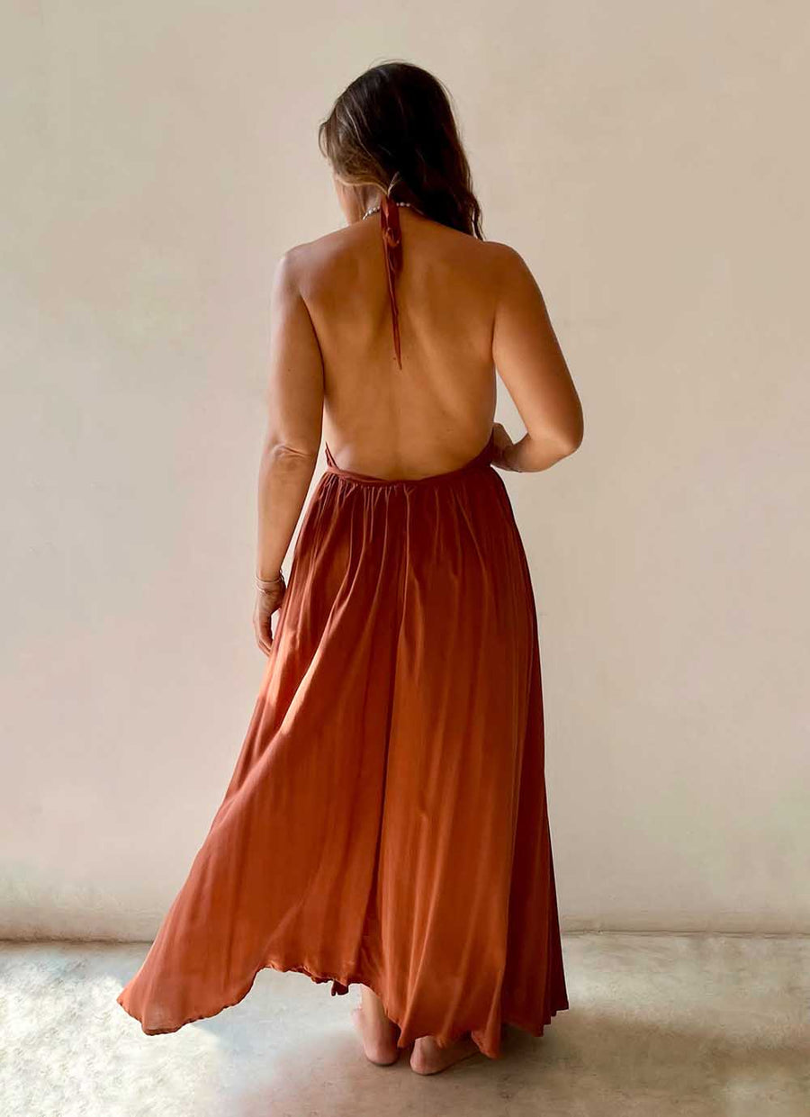 Woman wearing a rust-colored halter neck dress against a plain background