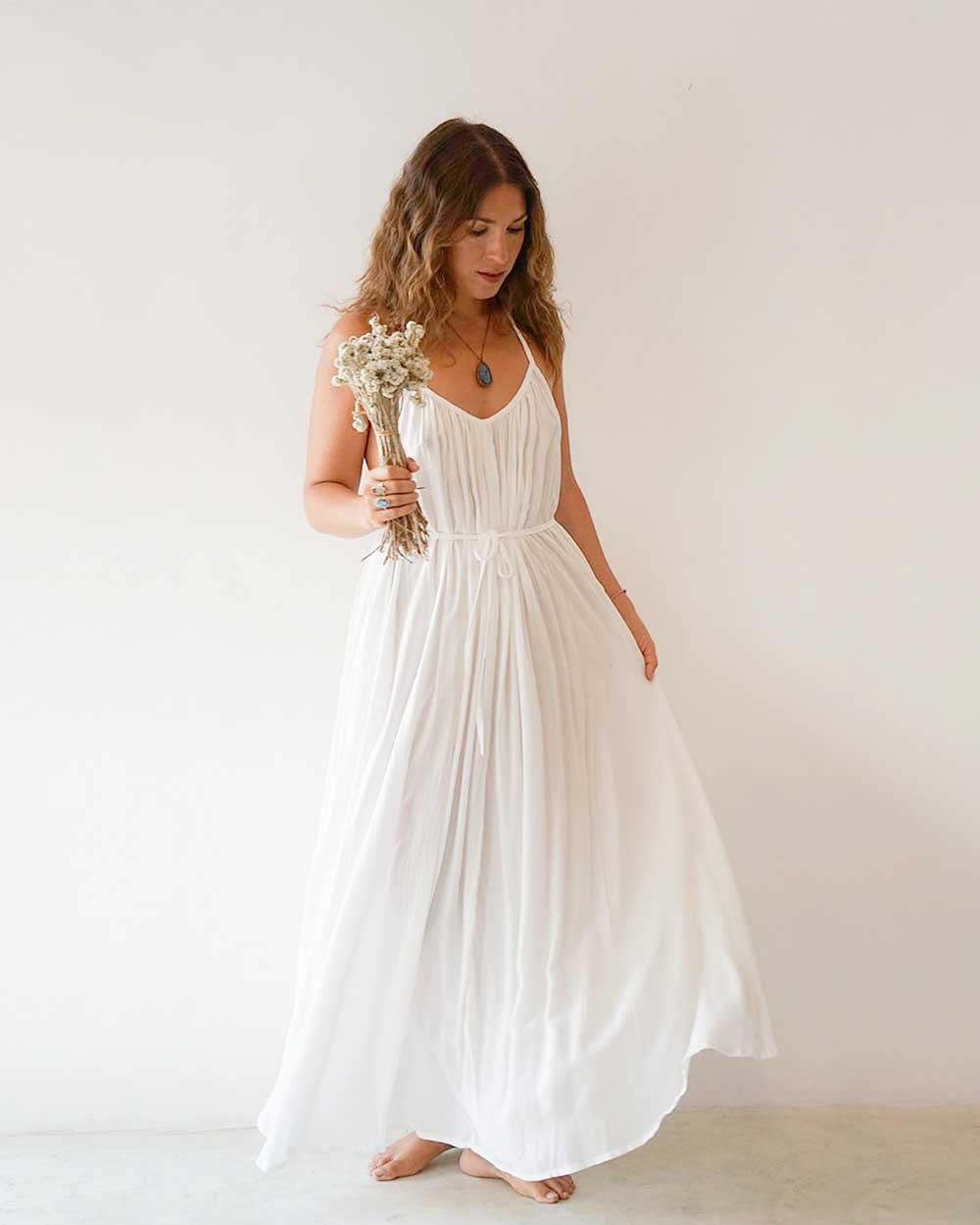 Woman in a white dress holding flowers against a plain background