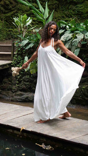 Woman in a white dress standing on a wooden platform with lush greenery in the background