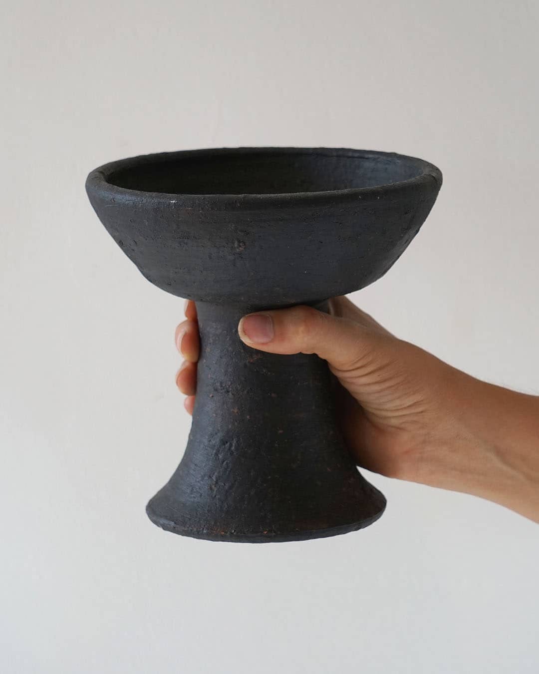 Hand holding a black ceramic bowl against a plain background