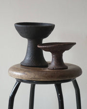 Two black ceramic bowls on a wooden stool against a plain background