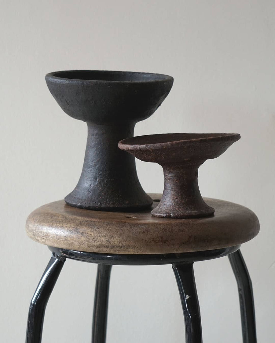 Two black ceramic bowls on a wooden stool against a plain background