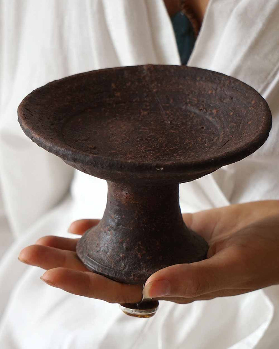 Person holding a dark brown ceramic dish against a white background