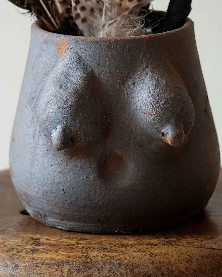 Ceramic planter shaped like a face with a plant inside on a wooden surface.