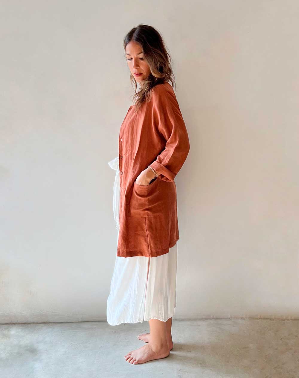 Woman wearing a rust-colored long shirt over a white dress against a plain background