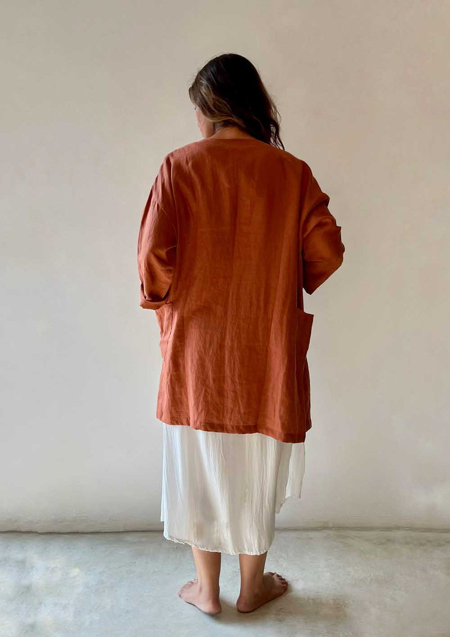 Person wearing a rust-colored shirt and white pants against a plain background