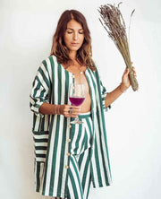 Woman in a green and white striped outfit holding a glass of wine and a bundle of dried herbs.