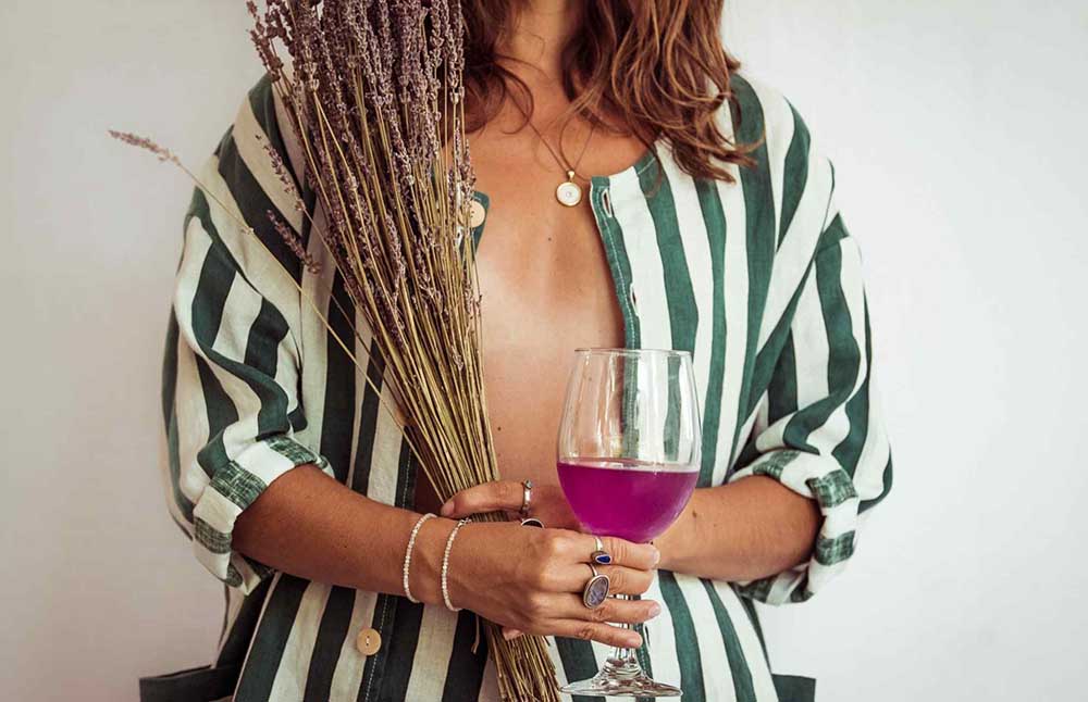 Person holding a glass of pink wine and a bundle of lavender.
