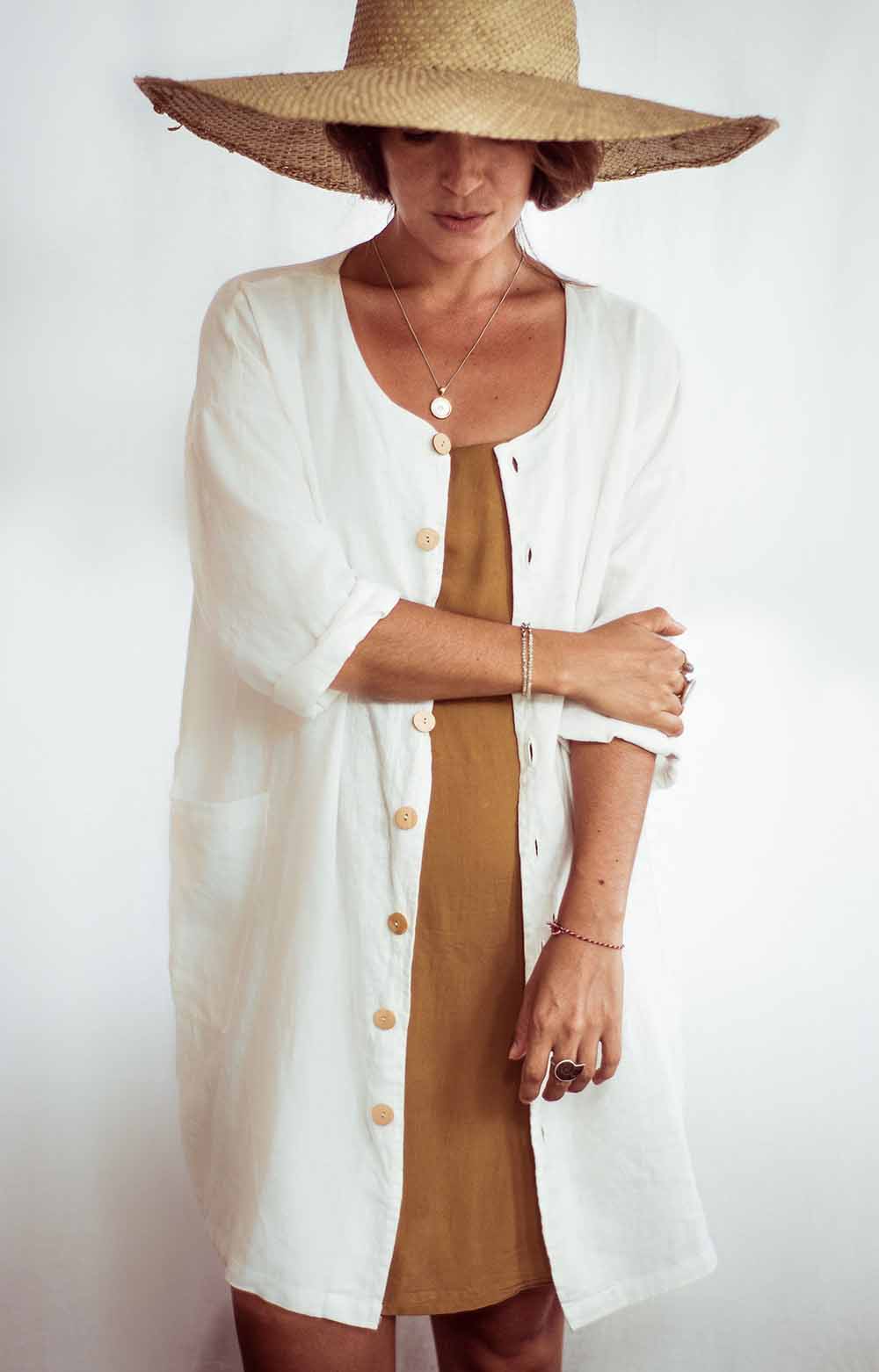 Woman wearing a white cardigan over a brown dress with a straw hat on a white background