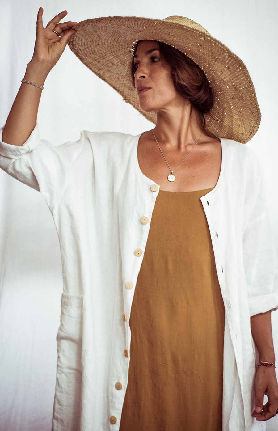 Woman wearing a straw hat, white cardigan, and brown dress against a white background